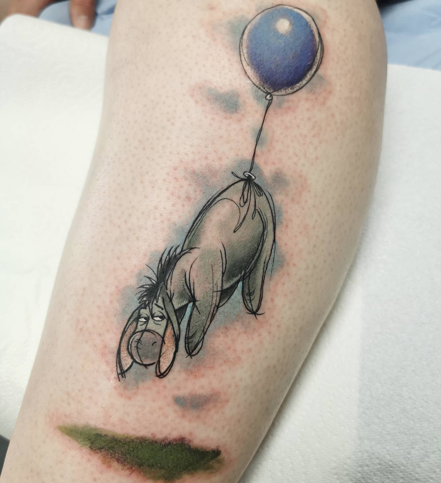 Tattoo of Eeyore from Winnie the Pooh hanging from a blue balloon with a melancholy expression